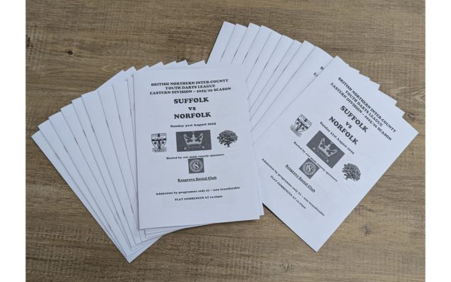 A stack of printed match day programmes for the Suffolk vs Norfolk Youth Darts League match.